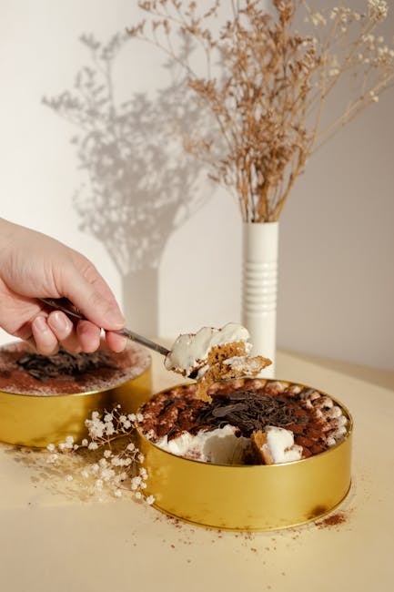 A stylish dessert scene with a hand holding a spoon to a cake in a sunlit room.
